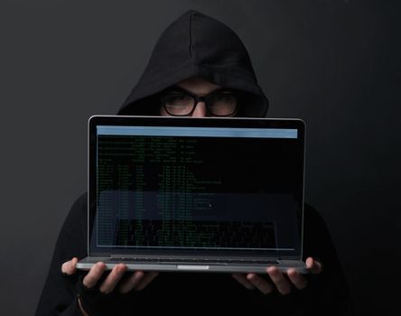 Im always watching. Portrait of an unidentifiable computer hacker holding up a laptop against a dark background.