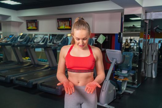 Young woman in sportswear having ache on palms after training in gym