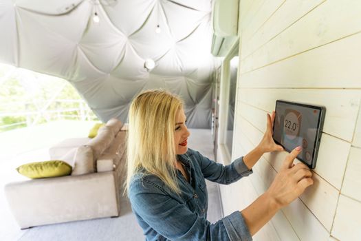 Young woman controlling home light with a digital tablet in the glamping dome tent. Concept of a smart home and light control with mobile devices