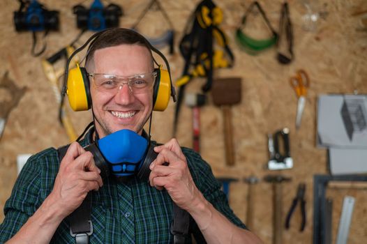 A carpenter in goggles and earmuffs removes a protective respirator.