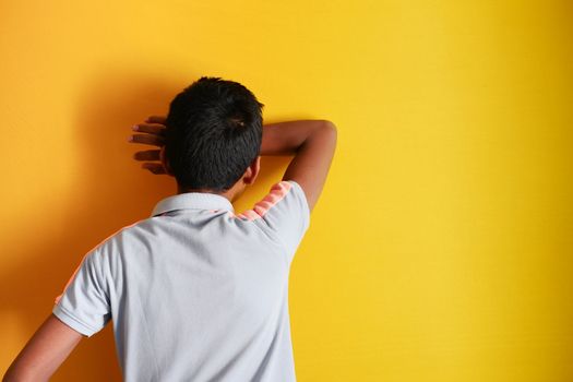 sad teenage boy covering his face on yellow background 