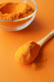 turmeric root powder on a wooden spoon on orange background 