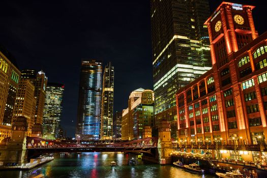 Buildings light up at night along Chicago ship canals with bridge