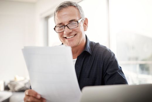 He keeps an accurate account of all his paperwork. a mature man going through some paperwork at home.