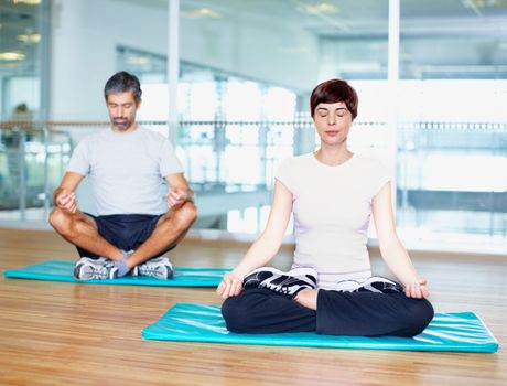 Meditating. Full length of woman and man in lotus positing meditating at gym.
