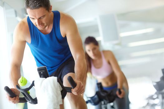 Hes got his eye on the prize. A man and woman exercising in spinning class at the gym.