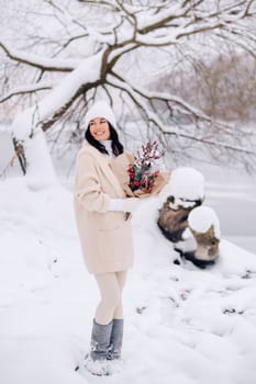 A girl in a beige cardigan and winter flowers walks in nature in the snowy season. Winter weather