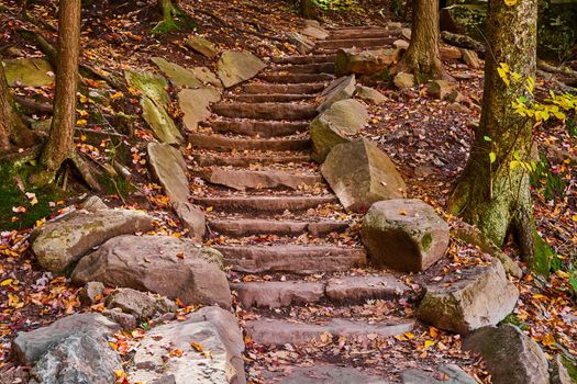 Hiking trail stone staircase line with boulders winds through fall forest