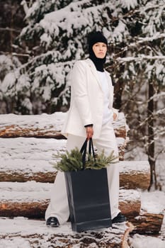 A girl in a white suit and balaclava with a package of Christmas trees in the winter forest on New Year's Eve.New Year's concept