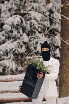 A girl in a white suit and balaclava with a package of Christmas trees in the winter forest on New Year's Eve.New Year's concept