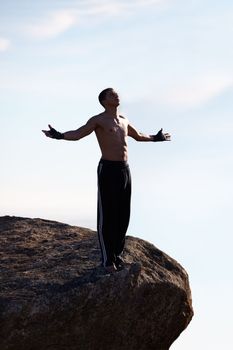 Freedom in the mountains. A male kickboxer looking upwards while standing on a mountain ledge.