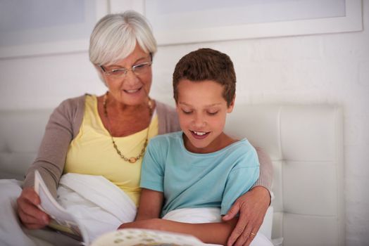 Story time with gran. A grandmother reading a book to her grandson in bed.