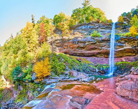 Vibrant bright HDR panorama of waterfall over cliffs with fall foliage