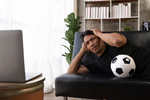 Young asian football fan disappointed and angry watching a football game on the couch