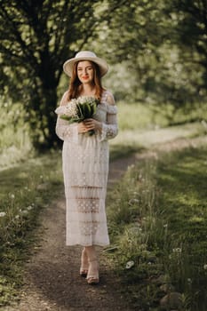 Portrait of a beautiful woman in a white dress and a hat with lilies of the valley. A girl in nature. Spring flowers