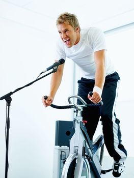Man enjoying work out at gym. Handsome man singing a song while cycling at the gym.