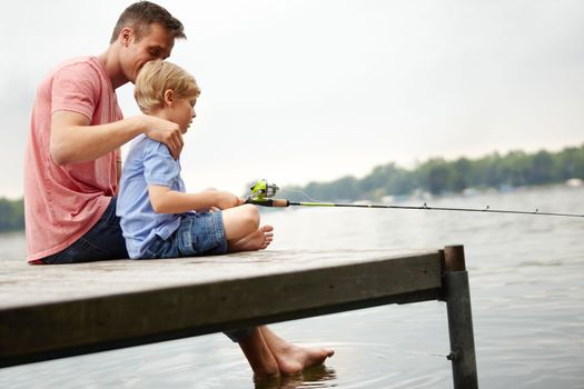 Teaching my son how to catch a fish. A father teaching his son how to fish whilst sitting on a ledge over a river with copyspace.