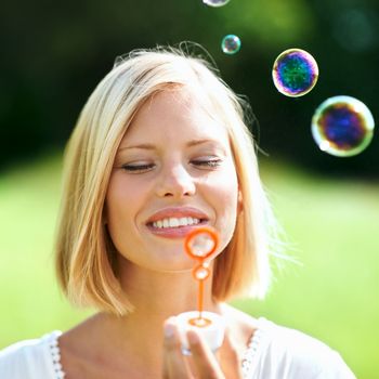 Having some innocent fun. Smiling young woman blowing soap bubbles outdoors.
