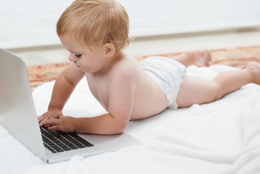 Technologically minded. Cute baby playing with a laptop while lying on the floor.