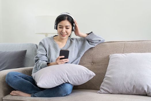 Asian woman listen music with mobile phone and headphones. Calm home weekend, relax while sit on sofa, enjoy favorite tune, popular music, use modern wireless headphones and gadgets in living room