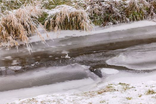 A frozen stream with ice and frost on reeds and grasses in winter, Germany