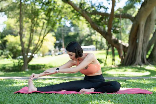 Young attractive girl is doing advanced yoga asana on the fitness mat in the middle of a park
