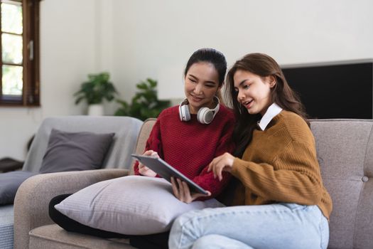Asian woman friends sitting in living room watching movie on tablet together. Modern female friendship enjoy weekend activity lifestyle with wireless technology at home