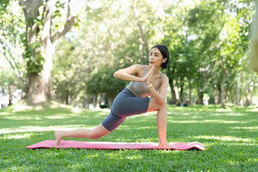 Young attractive girl is doing advanced yoga asana on the fitness mat in the middle of a park.
