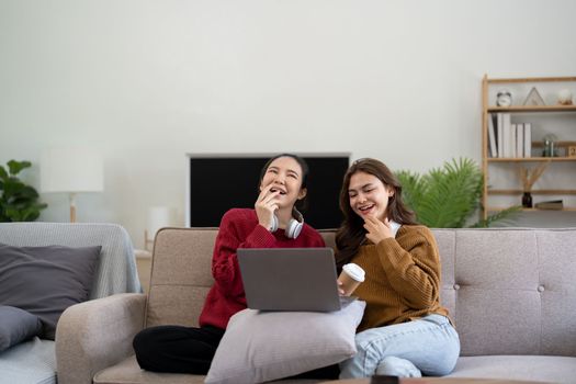 Asian woman friends sitting in living room watching movie on laptop together. Modern female friendship enjoy weekend activity lifestyle with wireless technology at home