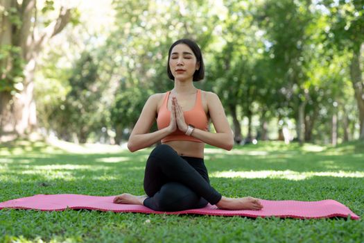 Yoga woman meditation praying outside in city park wellness. Summer exercise lifestyle active young Asian girl meditating background.