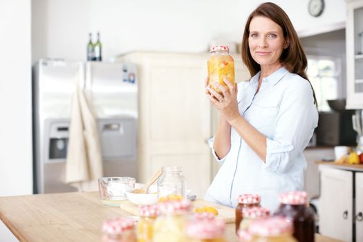 She takes pride in her work. A mature woman holding a jar of fruit in the kitchen.