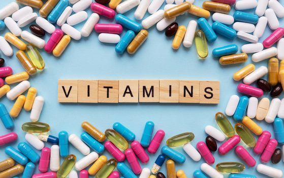 Different colorful pills from different symptoms in the middle - the inscription from wooden letters vitamins. Health and medicine concept.