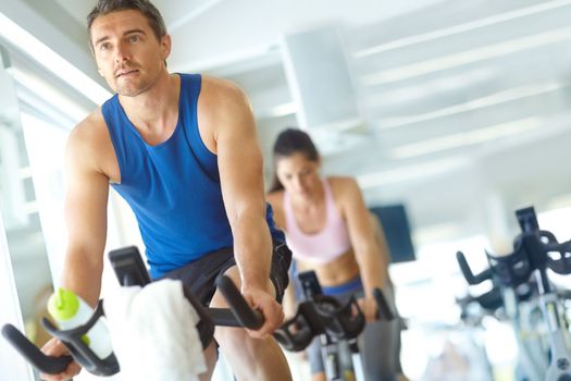 Spinning their way to toned bodies. A man and woman exercising in spinning class at the gym.