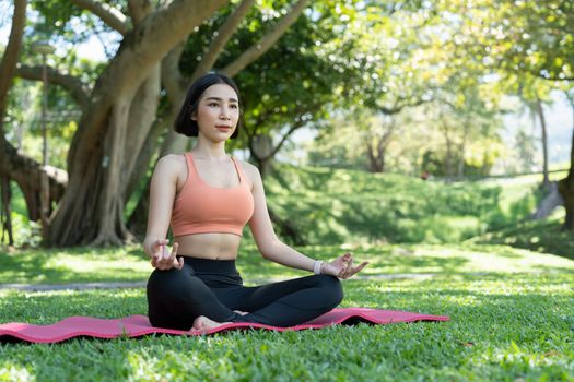 Yoga at park. Young asian woman in lotus pose sitting on green grass. Concept of calm and meditation.