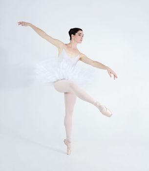 Each step expresses her love for dance. Elegant young ballerina dancing en pointe against a white background.