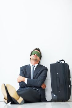 Nap time. Middle aged business man sitting against wall with travel luggage and taking a nap.