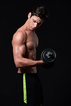 Pumping up his biceps. Studio shot of a young man working with dumbbells isolated on black.