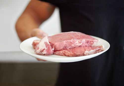 Ensuring his diet contains enough protein. Cropped image of a muscular man holding a plate of raw beef.