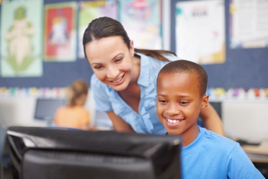 Enjoying computer class. A beautiful young woman helping out a young ethnic boy in computer class