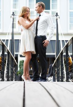 Playful pair. A beautiful woman stands on a bridge with her boyfriend and plays with his tie.