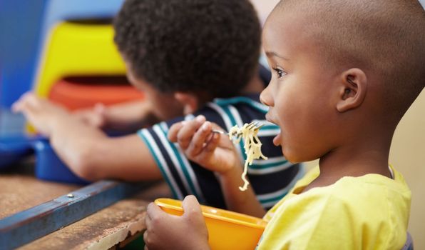 Enjoying a nutritious snack. Preschool african american boy sitting in his lunch break eating his noodles.