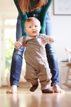 Taking one step at a time. Young mom helping her baby boy learn to walk.