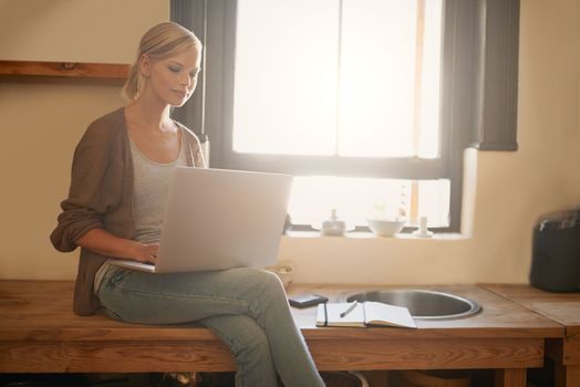 Finding the perfect dinner idea online. An attractive young woman using her laptop while sitting on her kitchen counter.