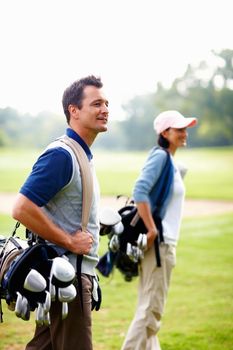 Man and woman carrying golf bags. Man and woman carrying golf bags and looking away.