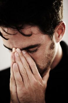 Praying desperately. A young man with his hands over his mouth in prayer.