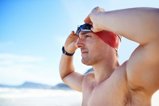 Preparing himself for his own record time. Cropped closeup shot of a man wearing swimming goggles looking out at the ocean.