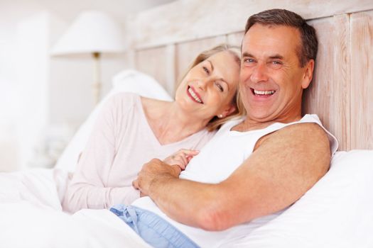 Cheerful mature man and wife spending time together in bed. Portrait of a cheerful mature man and wife spending time together in bed.
