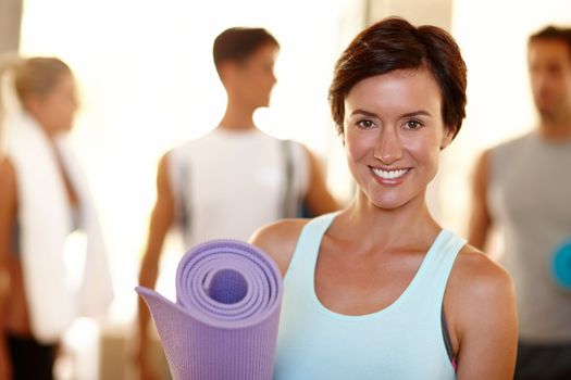Feeling good about my fitness commitment. Portrait of a beautiful woman with her yoga mat and people in the background.