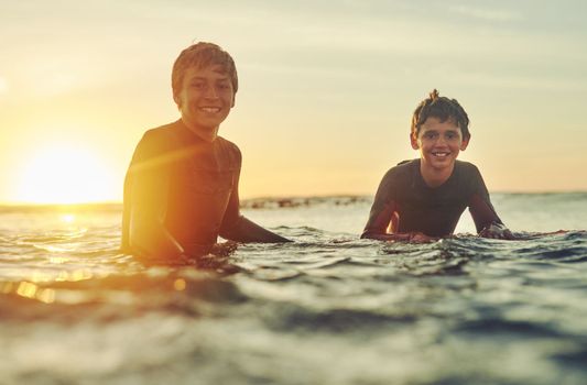 Surfs up. Portrait of two young brothers sitting on their surfboards in the ocean.