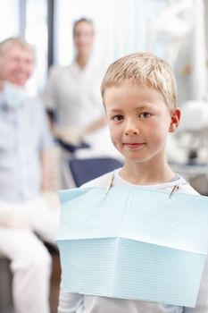 Smiling boy at dentists office. Portrait of cute young boy smiling with doctors in background.